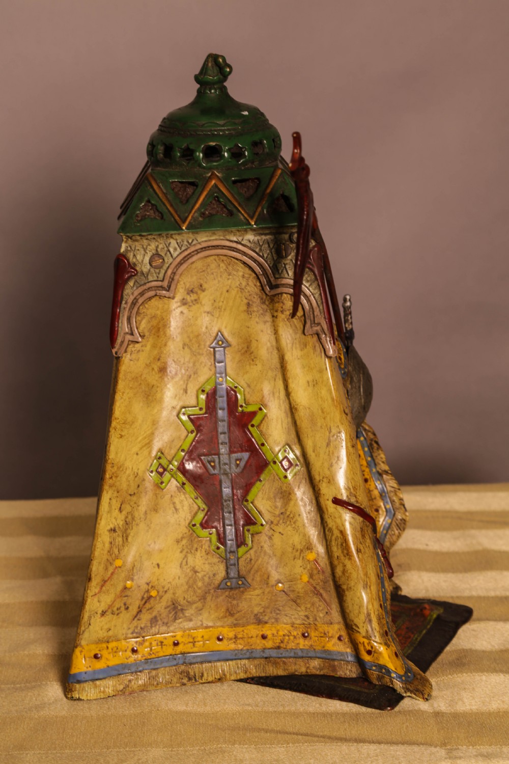 A cold-painted bronze sculpture depicting a bedouin tent with patterned yellow draping, a green domed top, and accompanying miniature weapons. View XI