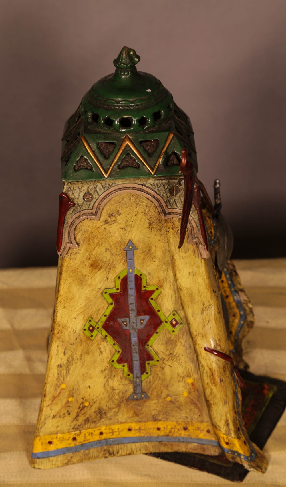 A cold-painted bronze sculpture depicting a bedouin tent with patterned yellow draping, a green domed top, and accompanying miniature weapons. View XII