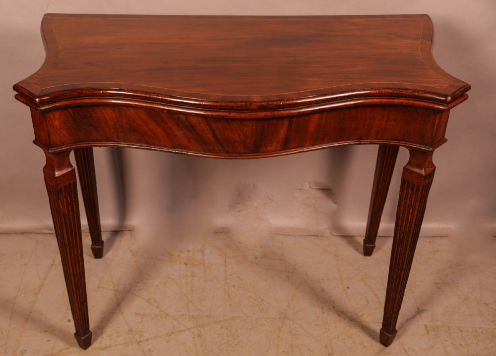 An 18th-century Georgian mahogany games table featuring a serpentine-curved folding top and fluted tapered legs.