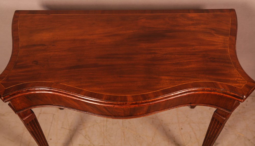 An 18th-century Georgian mahogany games table featuring a serpentine-curved folding top and fluted tapered legs. View II