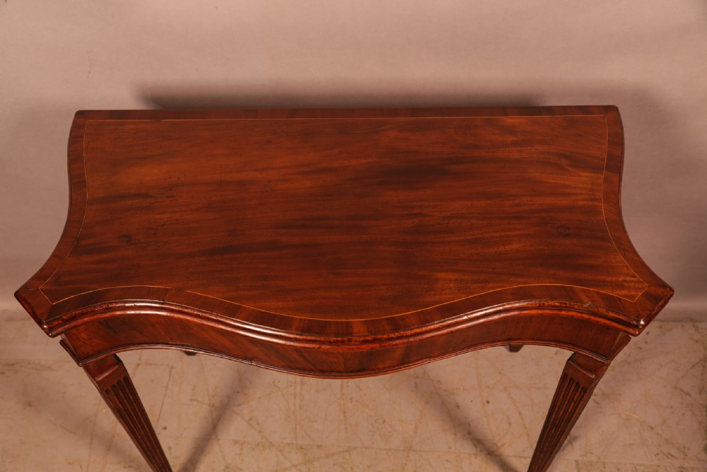 An 18th-century Georgian mahogany games table featuring a serpentine-curved folding top and fluted tapered legs. View III