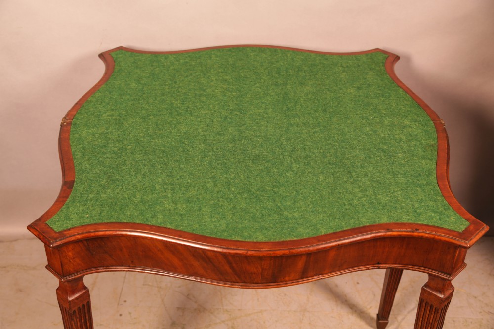 An 18th-century Georgian mahogany games table featuring a serpentine-curved folding top and fluted tapered legs. View V