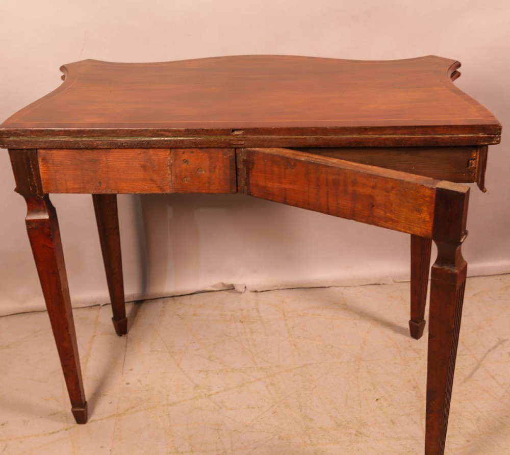 An 18th-century Georgian mahogany games table featuring a serpentine-curved folding top and fluted tapered legs. View X