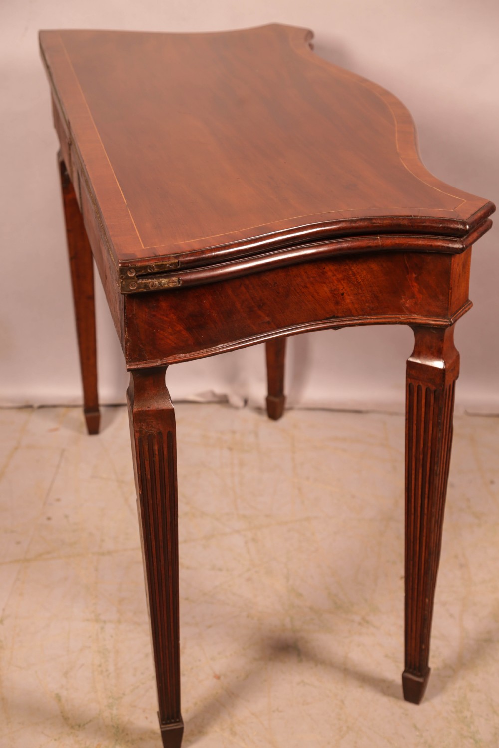 An 18th-century Georgian mahogany games table featuring a serpentine-curved folding top and fluted tapered legs. View XI
