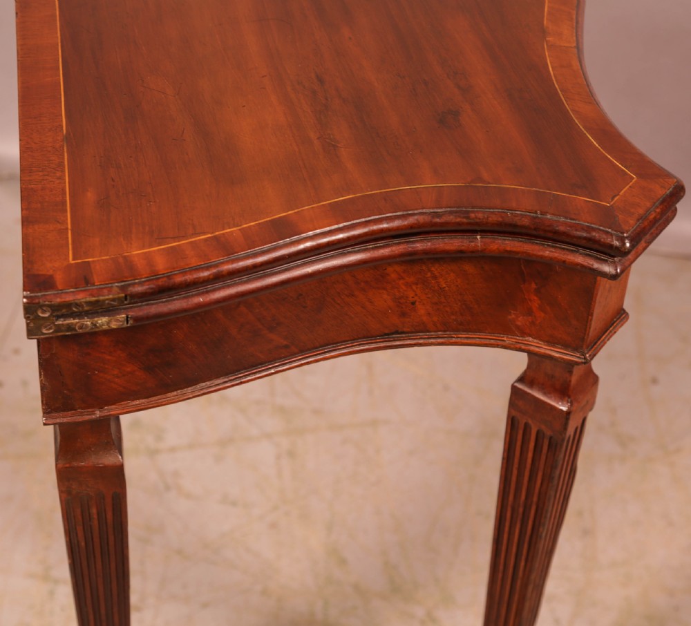 An 18th-century Georgian mahogany games table featuring a serpentine-curved folding top and fluted tapered legs. View XII