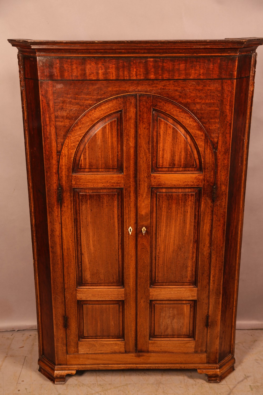 An 18th-century freestanding mahogany corner cupboard featuring arched double panel doors, keyhole escutcheons, and bracket feet. View II