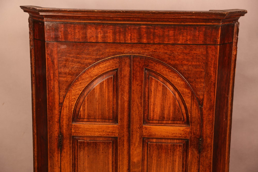 An 18th-century freestanding mahogany corner cupboard featuring arched double panel doors, keyhole escutcheons, and bracket feet. View III