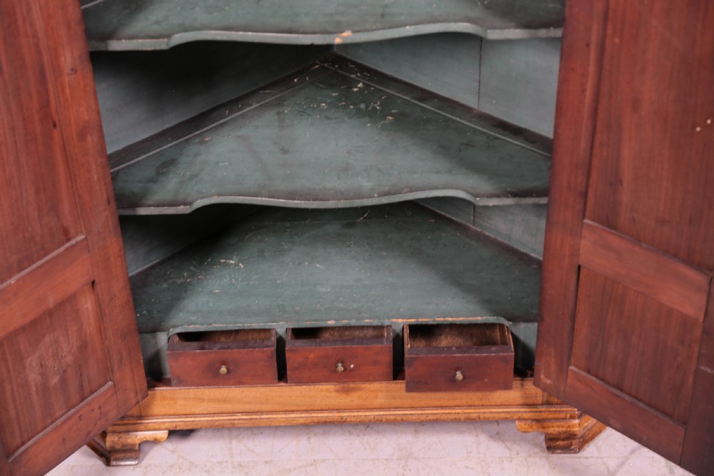 An 18th-century freestanding mahogany corner cupboard featuring arched double panel doors, keyhole escutcheons, and bracket feet. View V