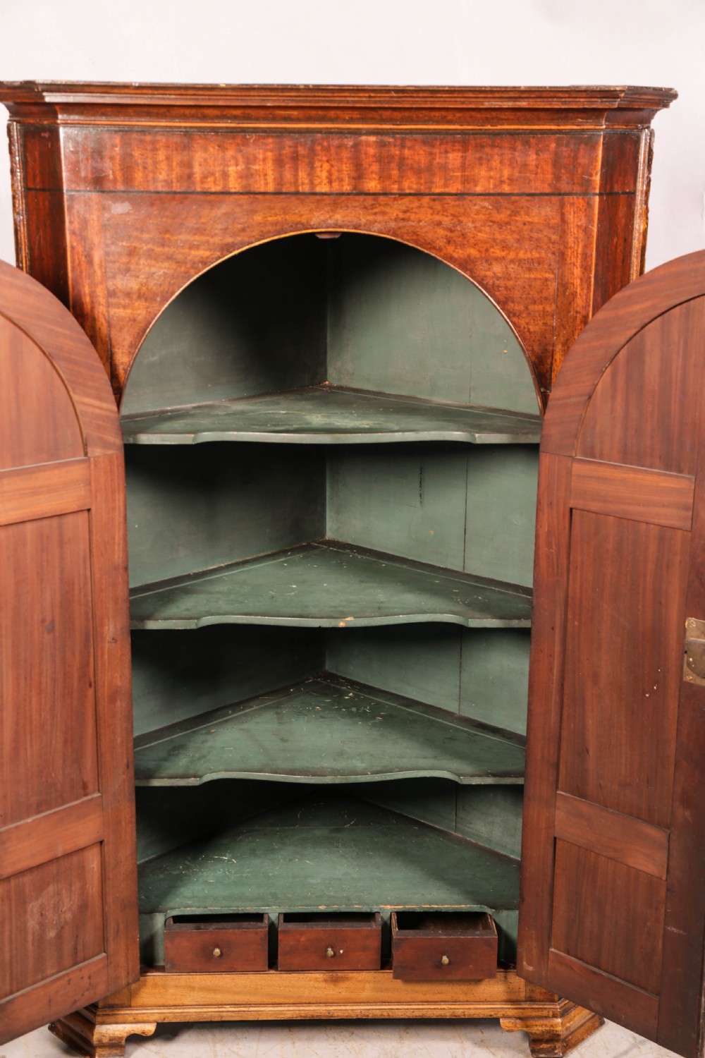 An 18th-century freestanding mahogany corner cupboard featuring arched double panel doors, keyhole escutcheons, and bracket feet. View VI