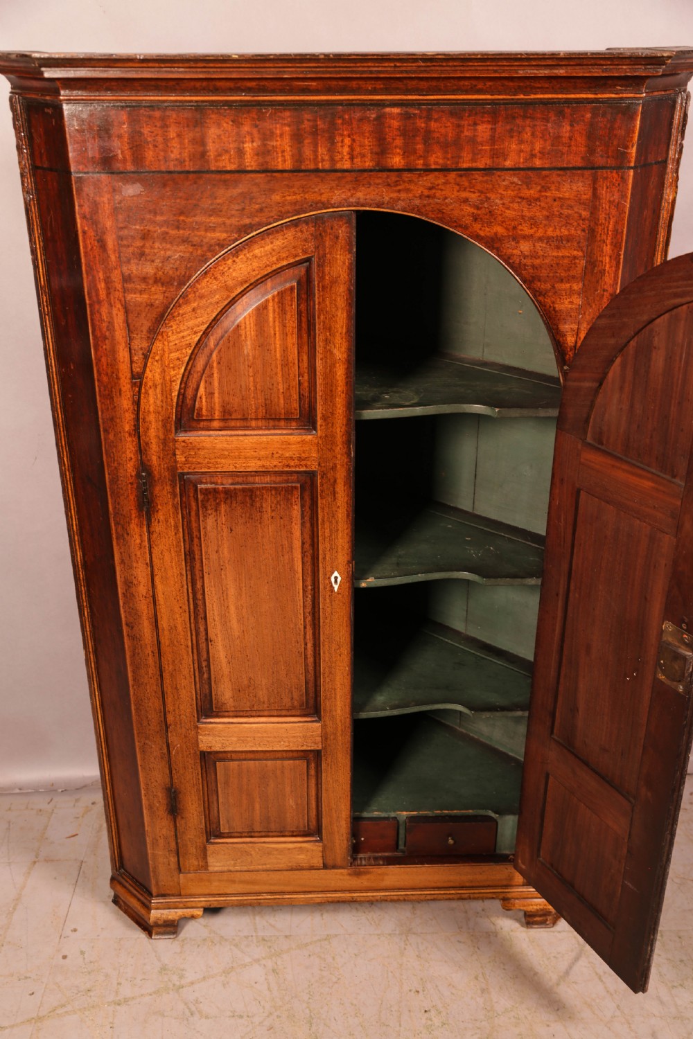 An 18th-century freestanding mahogany corner cupboard featuring arched double panel doors, keyhole escutcheons, and bracket feet. View IX