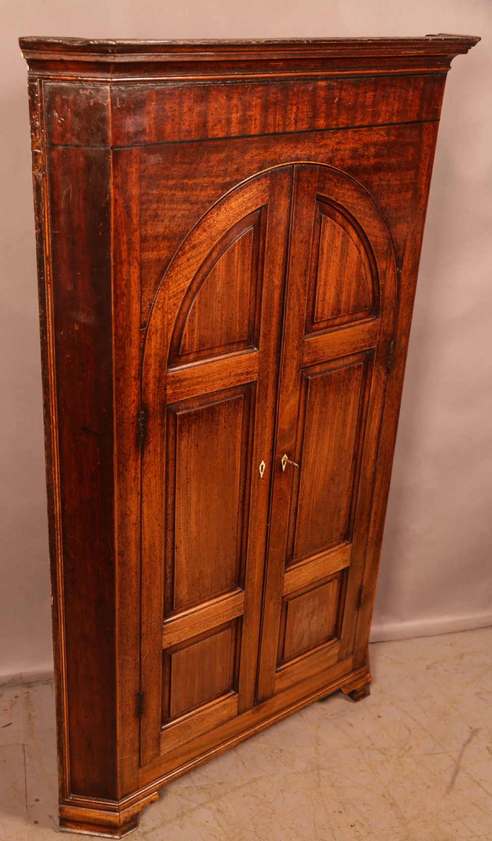 An 18th-century freestanding mahogany corner cupboard featuring arched double panel doors, keyhole escutcheons, and bracket feet. View X