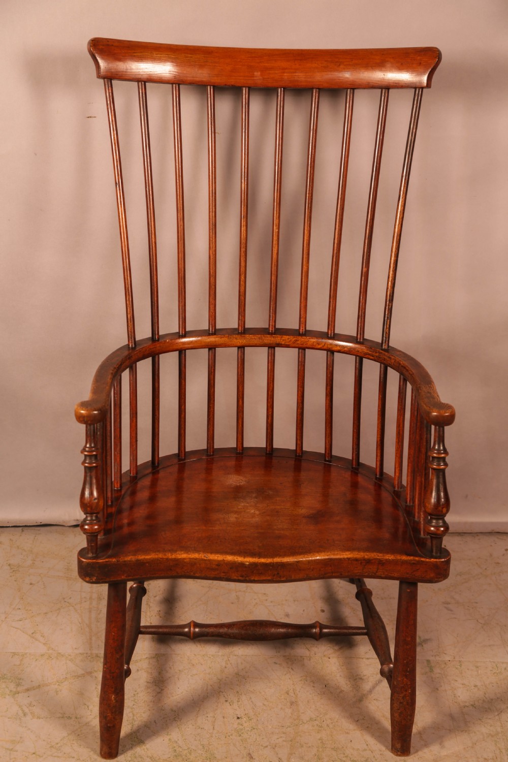 A high-back Scottish Darvel Windsor armchair crafted from warm brown wood, featuring a comb crest rail, spindle back, curved arm bow, and saddle seat.