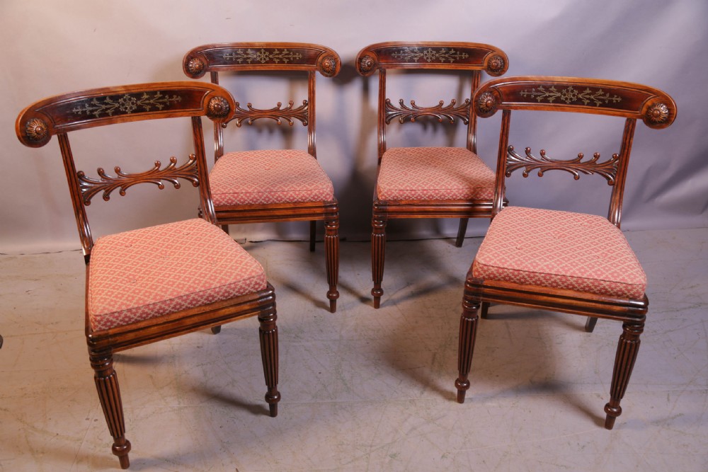 A set of four Regency rosewood dining chairs featuring brass inlay on the curved crest rails, carved splats, reeded front legs, and patterned red seats.