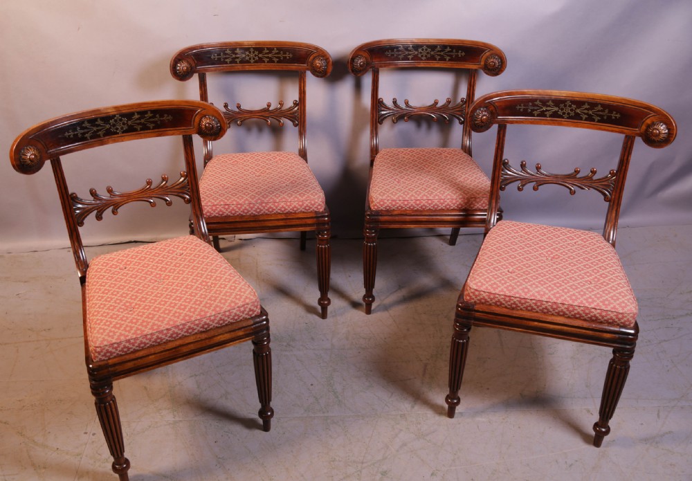 A set of four Regency rosewood dining chairs featuring brass inlay on the curved crest rails, carved splats, reeded front legs, and patterned red seats. View II