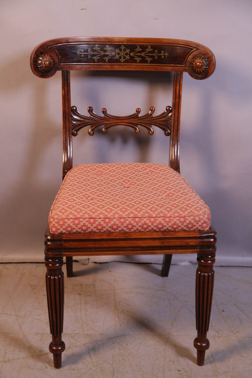 A set of four Regency rosewood dining chairs featuring brass inlay on the curved crest rails, carved splats, reeded front legs, and patterned red seats. View III