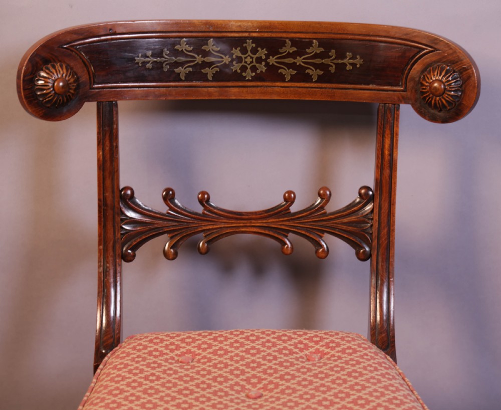 A set of four Regency rosewood dining chairs featuring brass inlay on the curved crest rails, carved splats, reeded front legs, and patterned red seats. View V