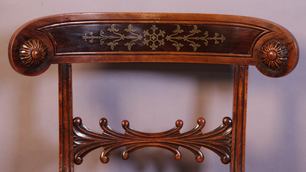 A set of four Regency rosewood dining chairs featuring brass inlay on the curved crest rails, carved splats, reeded front legs, and patterned red seats. View VI
