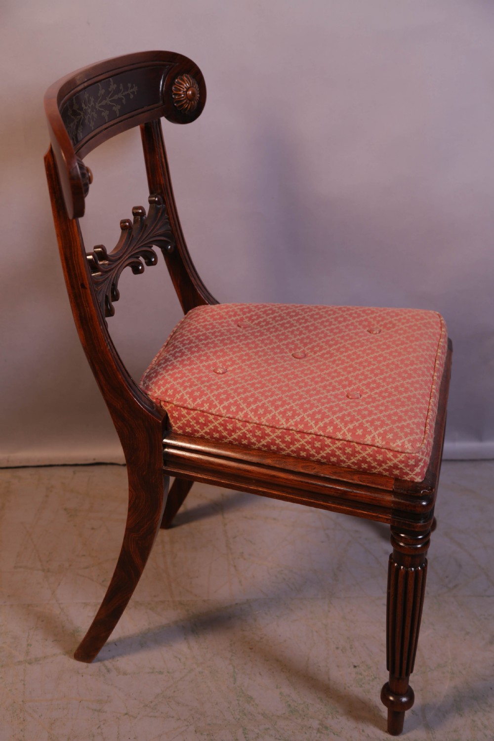 A set of four Regency rosewood dining chairs featuring brass inlay on the curved crest rails, carved splats, reeded front legs, and patterned red seats. View IX