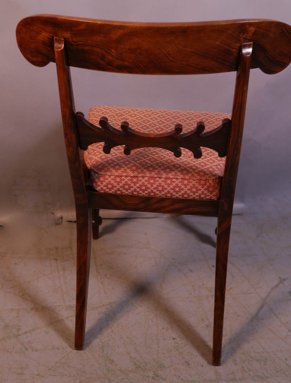 A set of four Regency rosewood dining chairs featuring brass inlay on the curved crest rails, carved splats, reeded front legs, and patterned red seats. View X