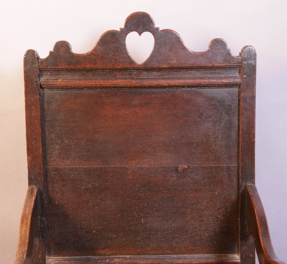 A dark oak 17th-century wainscot armchair featuring a panelled backrest with a shaped crest rail, curved armrests, and turned front legs. View III