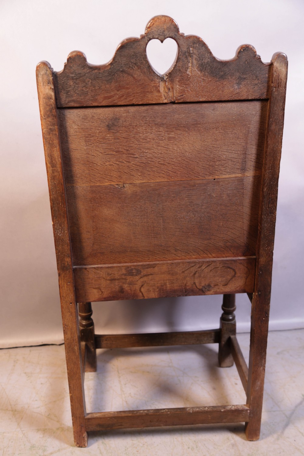 A dark oak 17th-century wainscot armchair featuring a panelled backrest with a shaped crest rail, curved armrests, and turned front legs. View IV