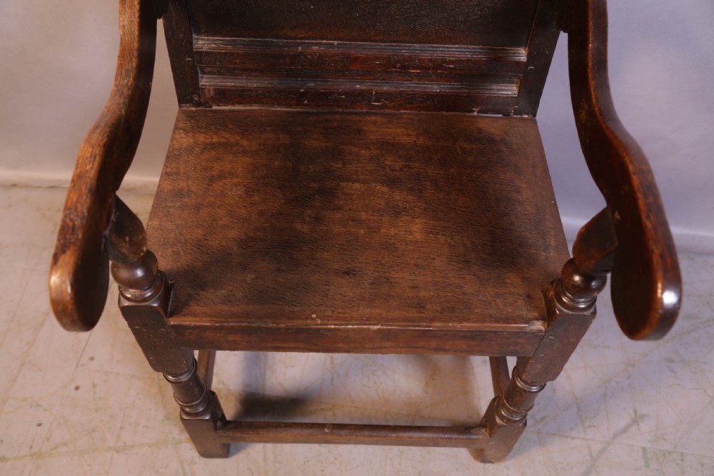 A dark oak 17th-century wainscot armchair featuring a panelled backrest with a shaped crest rail, curved armrests, and turned front legs. View VI
