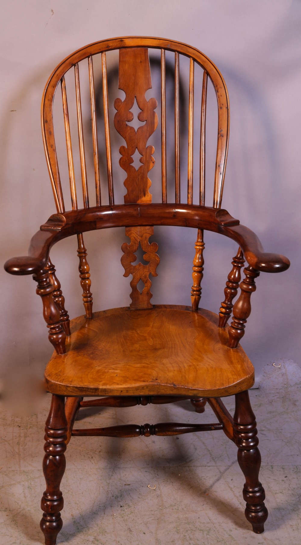 A warm brown yew wood Windsor chair with a hoop back, central pierced splat, wide armrests, turned legs, and H-stretcher supports. View III