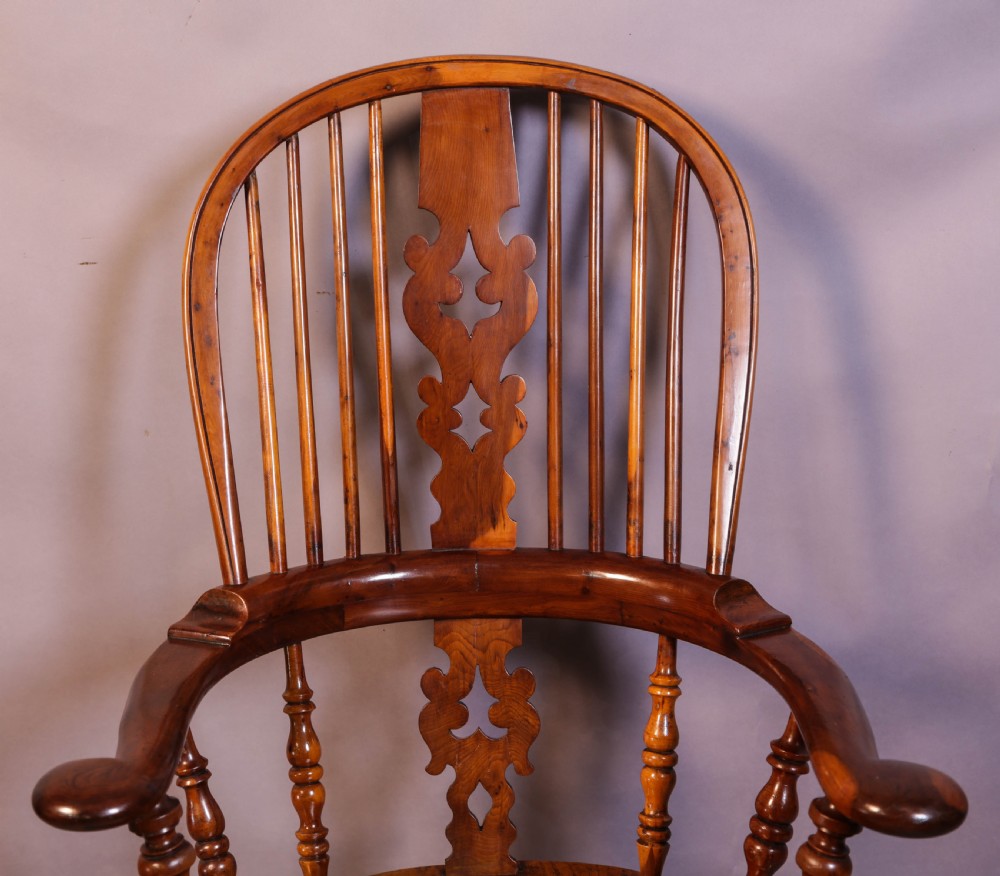 A warm brown yew wood Windsor chair with a hoop back, central pierced splat, wide armrests, turned legs, and H-stretcher supports. View IV
