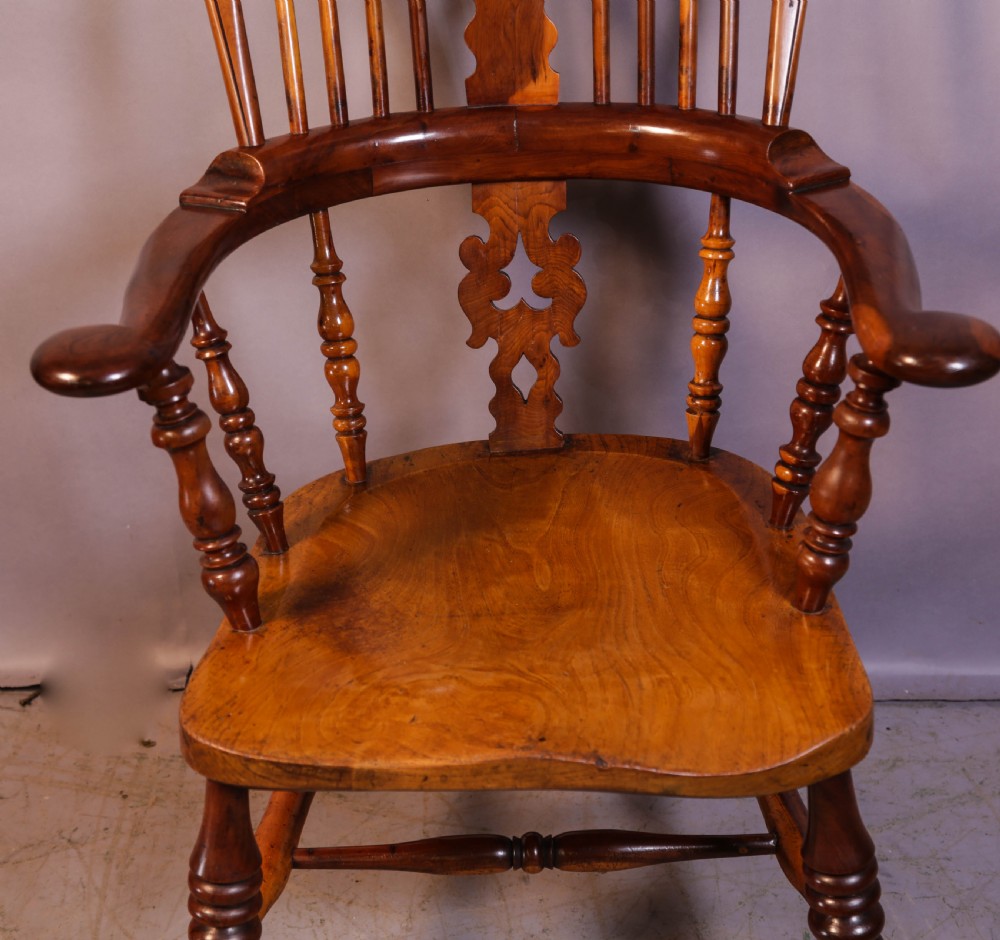 A warm brown yew wood Windsor chair with a hoop back, central pierced splat, wide armrests, turned legs, and H-stretcher supports. View V