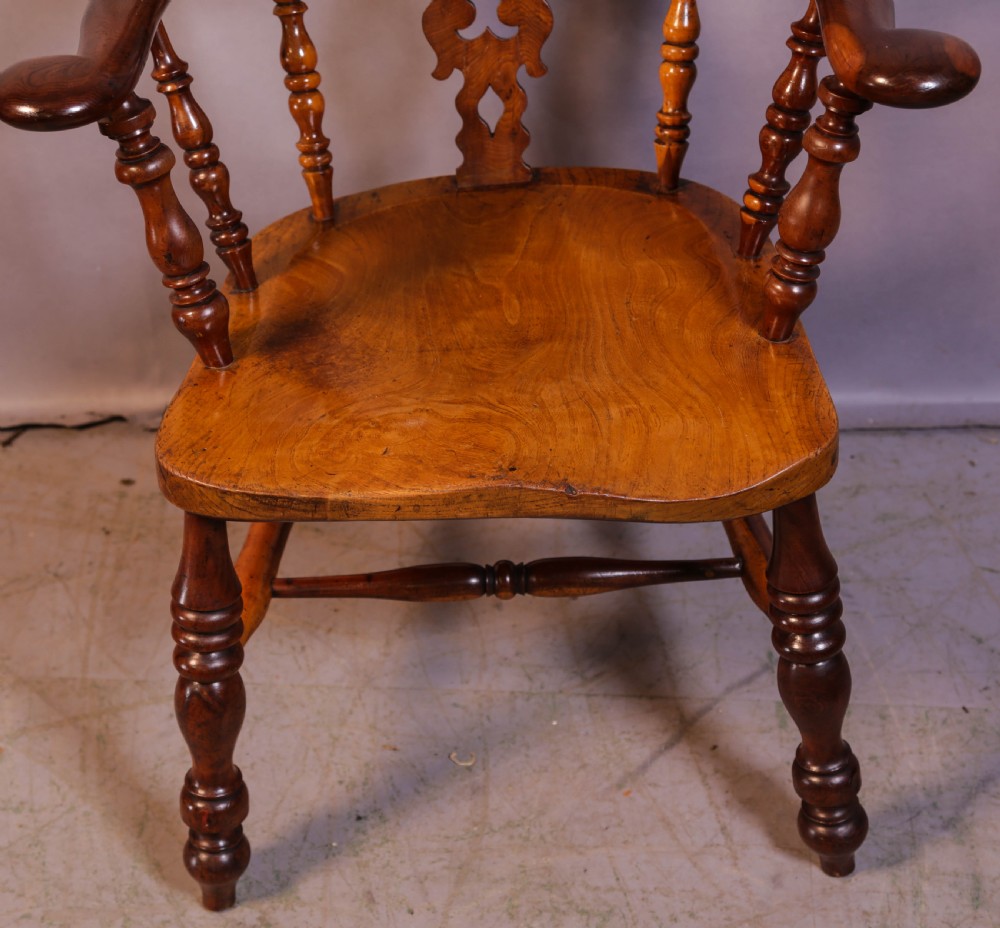 A warm brown yew wood Windsor chair with a hoop back, central pierced splat, wide armrests, turned legs, and H-stretcher supports. View VI