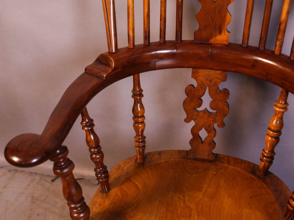 A warm brown yew wood Windsor chair with a hoop back, central pierced splat, wide armrests, turned legs, and H-stretcher supports. View VII