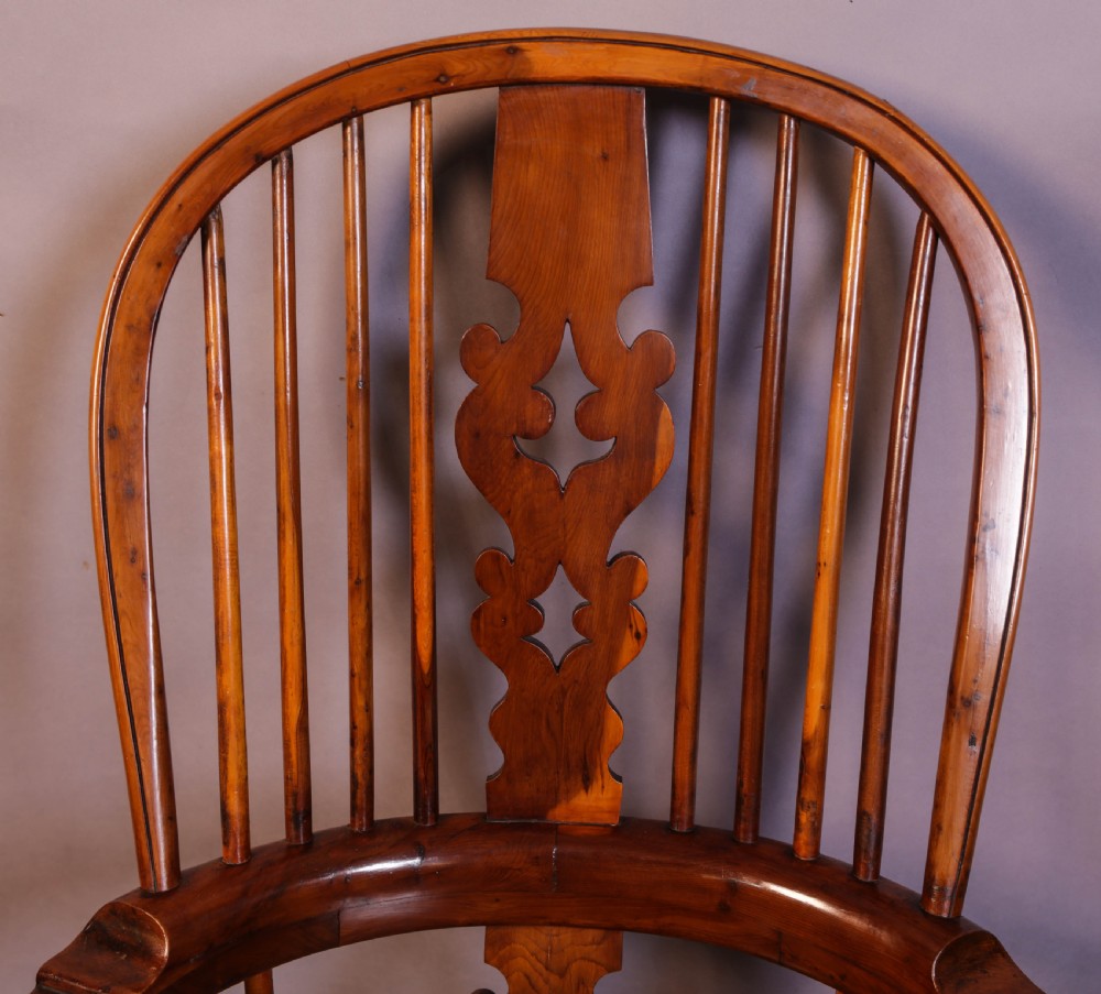 A warm brown yew wood Windsor chair with a hoop back, central pierced splat, wide armrests, turned legs, and H-stretcher supports. View X