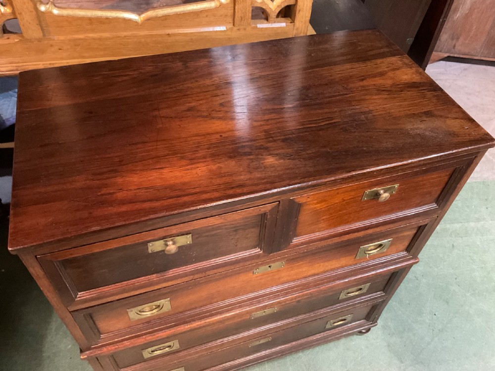 An antique padouk wood campaign chest of drawers featuring two short over three long drawers with recessed brass handles and turned feet. View II