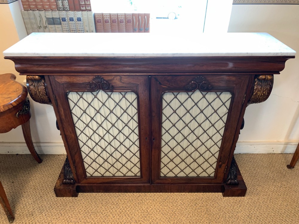 A dark rosewood chiffonier featuring a white marble top, carved gilt corbels, and two cupboard doors with pleated fabric behind a wooden lattice. View VII
