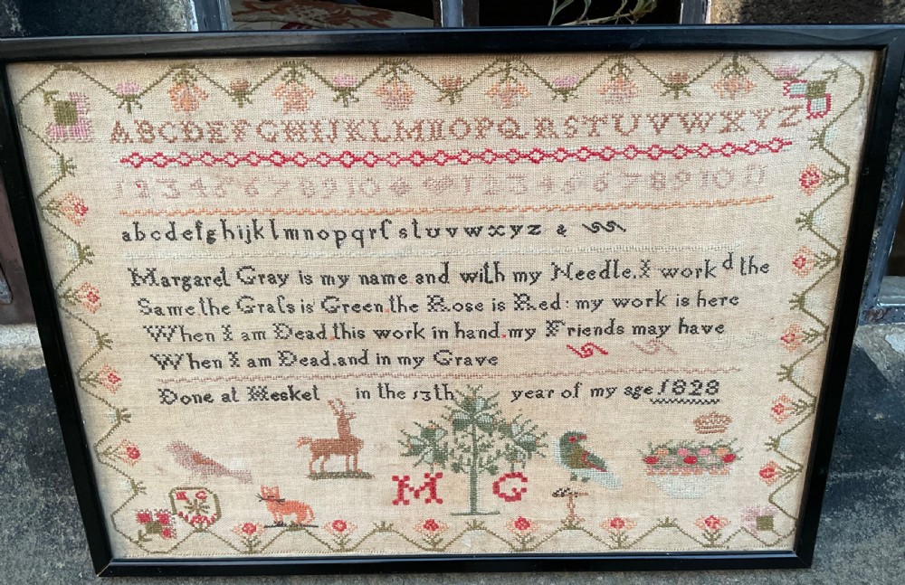 A framed antique Georgian needlework sampler featuring alphabets, numbers, a stitched verse, and various motifs including a central tree, animals, and floral borders on a neutral linen background.
