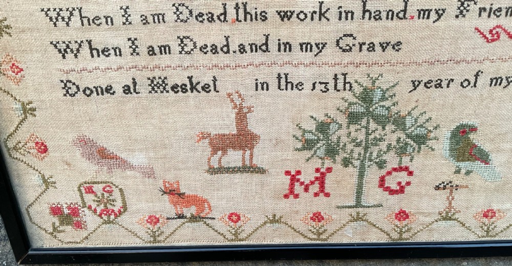 A framed antique Georgian needlework sampler featuring alphabets, numbers, a stitched verse, and various motifs including a central tree, animals, and floral borders on a neutral linen background. View II