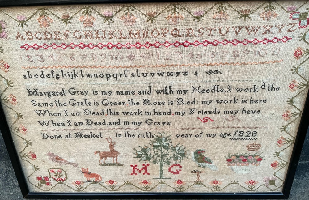A framed antique Georgian needlework sampler featuring alphabets, numbers, a stitched verse, and various motifs including a central tree, animals, and floral borders on a neutral linen background. View IV