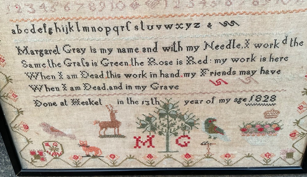 A framed antique Georgian needlework sampler featuring alphabets, numbers, a stitched verse, and various motifs including a central tree, animals, and floral borders on a neutral linen background. View V