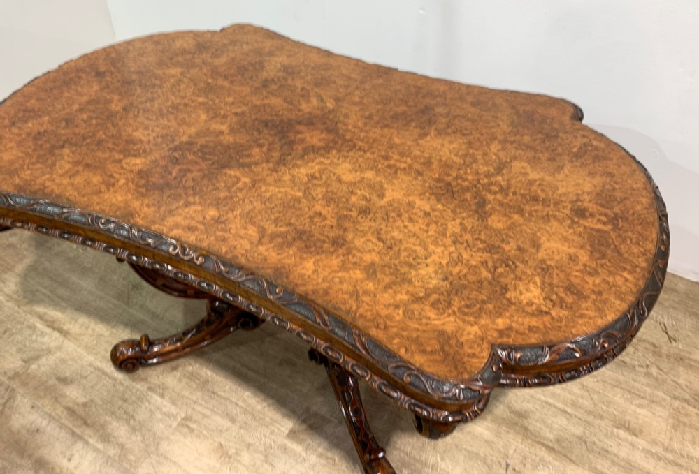 A rectangular Victorian burr walnut centre table with a figured top, carved edges, and a multi-scroll pedestal base. View II