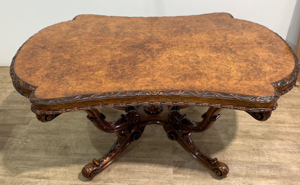 A rectangular Victorian burr walnut centre table with a figured top, carved edges, and a multi-scroll pedestal base. View VI