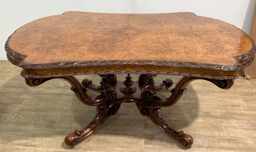 A rectangular Victorian burr walnut centre table with a figured top, carved edges, and a multi-scroll pedestal base. View VII
