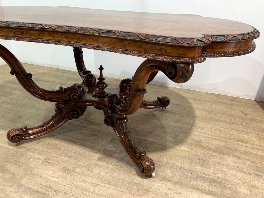 A rectangular Victorian burr walnut centre table with a figured top, carved edges, and a multi-scroll pedestal base. View XI