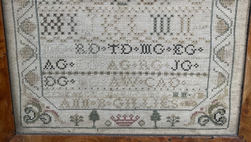 An antique hand-stitched needlework sampler displaying alphabets, numerals, coronet motifs, and the name Ann B Gillies inside a broad burr wood frame. View II