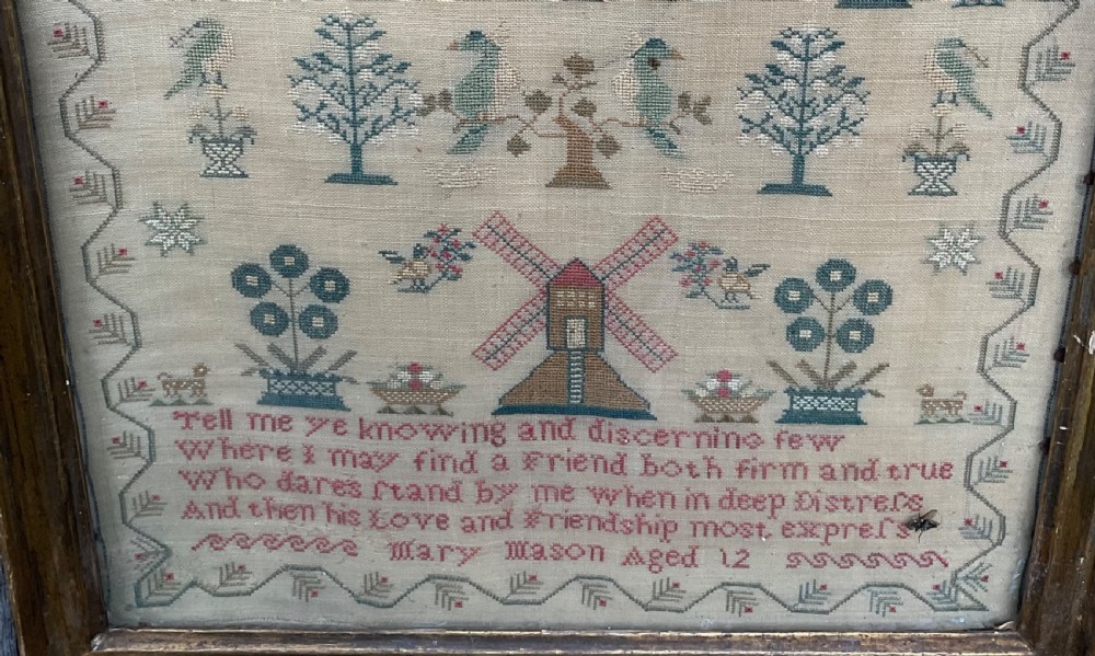 A framed antique needlework sampler on cream linen featuring embroidered trees, stags, flowers, a central windmill, a poetic verse, and the makers signature Mary Mason Aged 12. View II