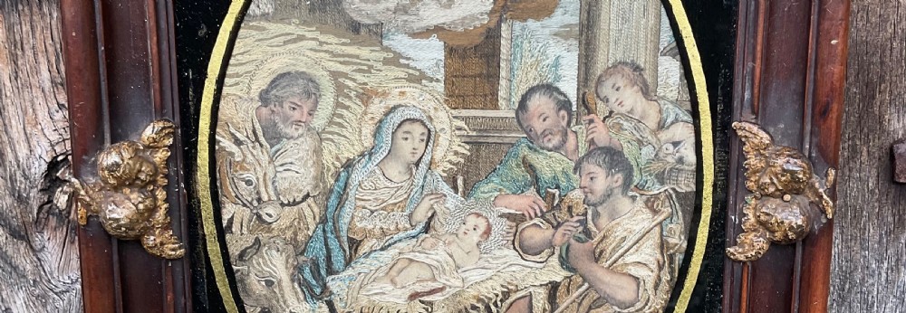 An eighteenth-century oval silk needlework depicting the Nativity scene, set within a black glass mat with gold star accents and a dark carved wood frame with gilt ornaments. View III