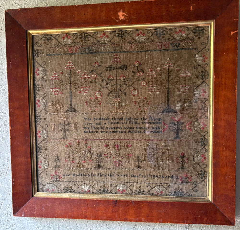 Framed Victorian needlework sampler featuring embroidered alphabets, floral motifs, a central verse, and a signature line dated 1847 set within a wide wooden frame.