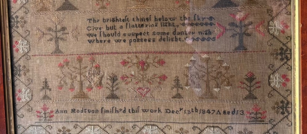 Framed Victorian needlework sampler featuring embroidered alphabets, floral motifs, a central verse, and a signature line dated 1847 set within a wide wooden frame. View III