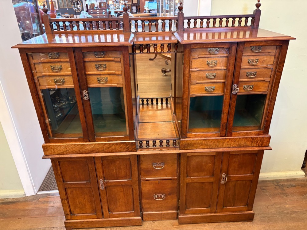 A Victorian walnut collectors cabinet featuring glazed upper doors revealing shallow specimen drawers, a spindled top gallery, a central mirrored recess, and a lower panelled cupboard base with brass handles.