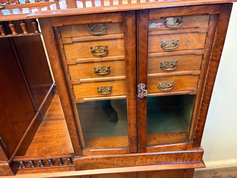 A Victorian walnut collectors cabinet featuring glazed upper doors revealing shallow specimen drawers, a spindled top gallery, a central mirrored recess, and a lower panelled cupboard base with brass handles. View III