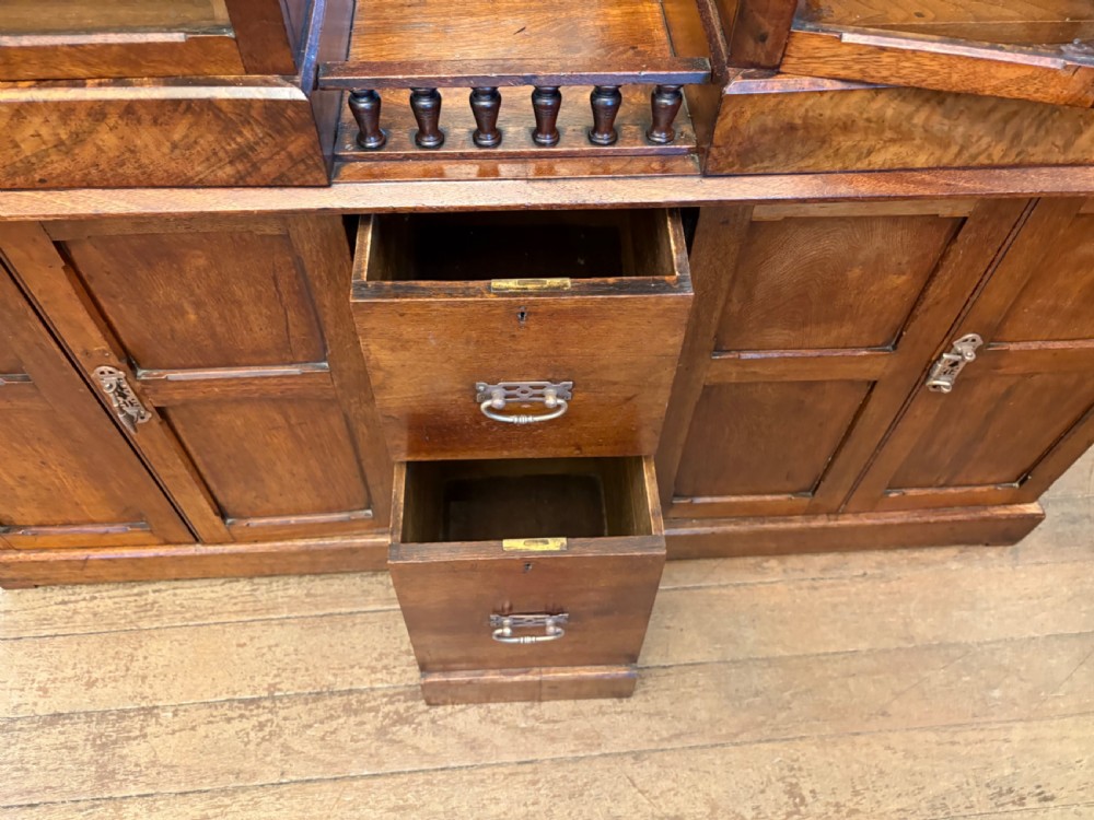 A Victorian walnut collectors cabinet featuring glazed upper doors revealing shallow specimen drawers, a spindled top gallery, a central mirrored recess, and a lower panelled cupboard base with brass handles. View VII